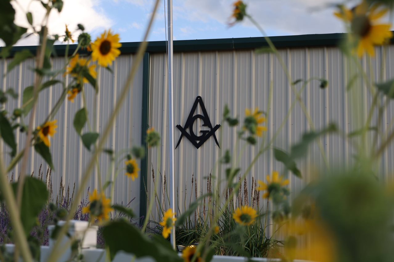 Masonic symbol on the side of a metal building with sunflowers in the foreground.